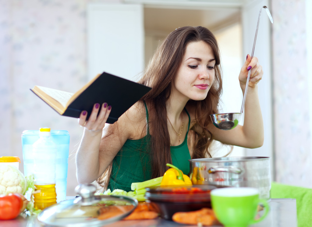 housewife cooking with ladle and cookbook in kitchen