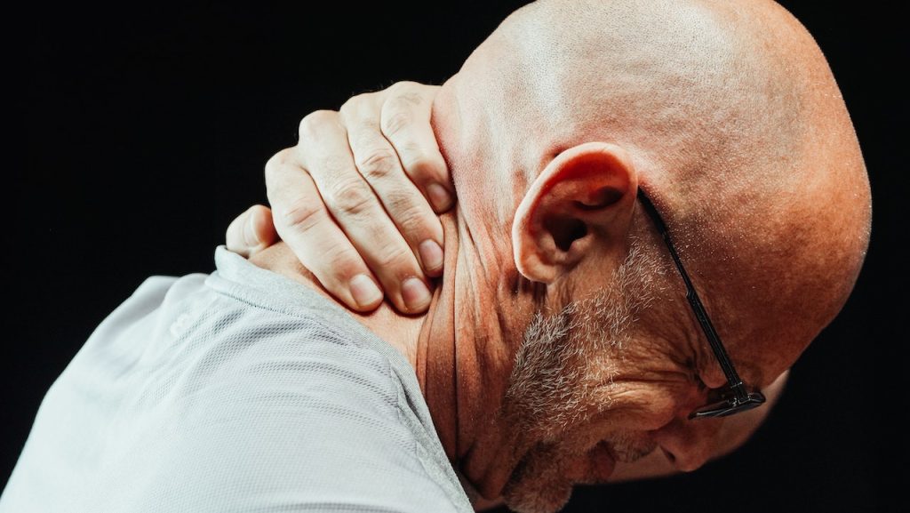 bald man holding neck in pain