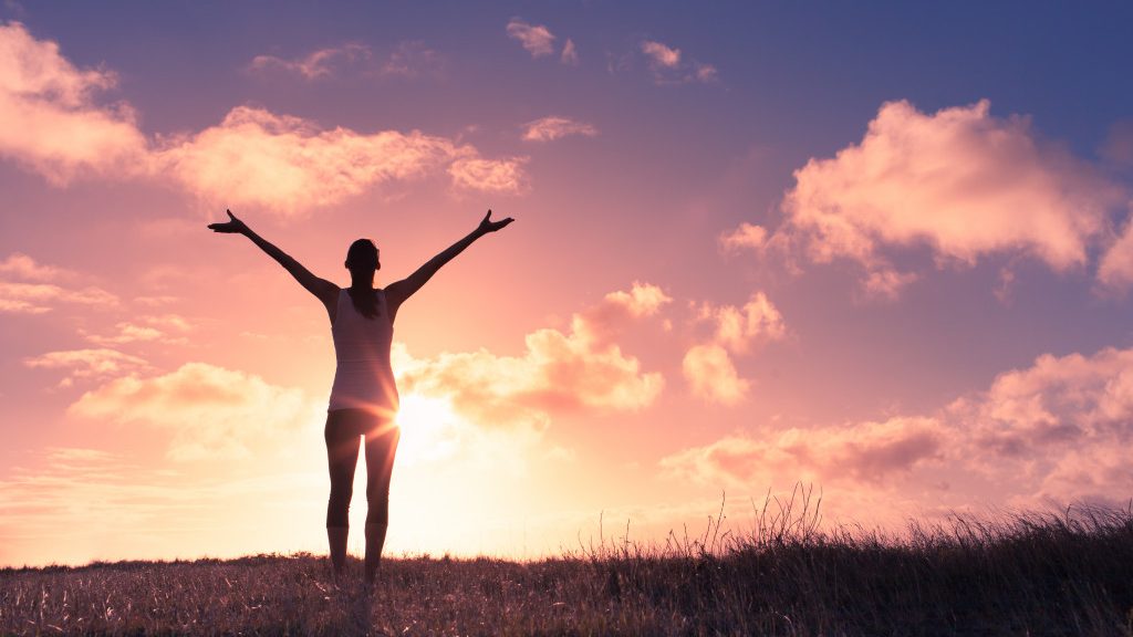 A content woman with her arm wide open in an indigo sunset background