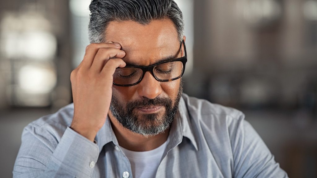 a senior man with hands on head feeling dizzy