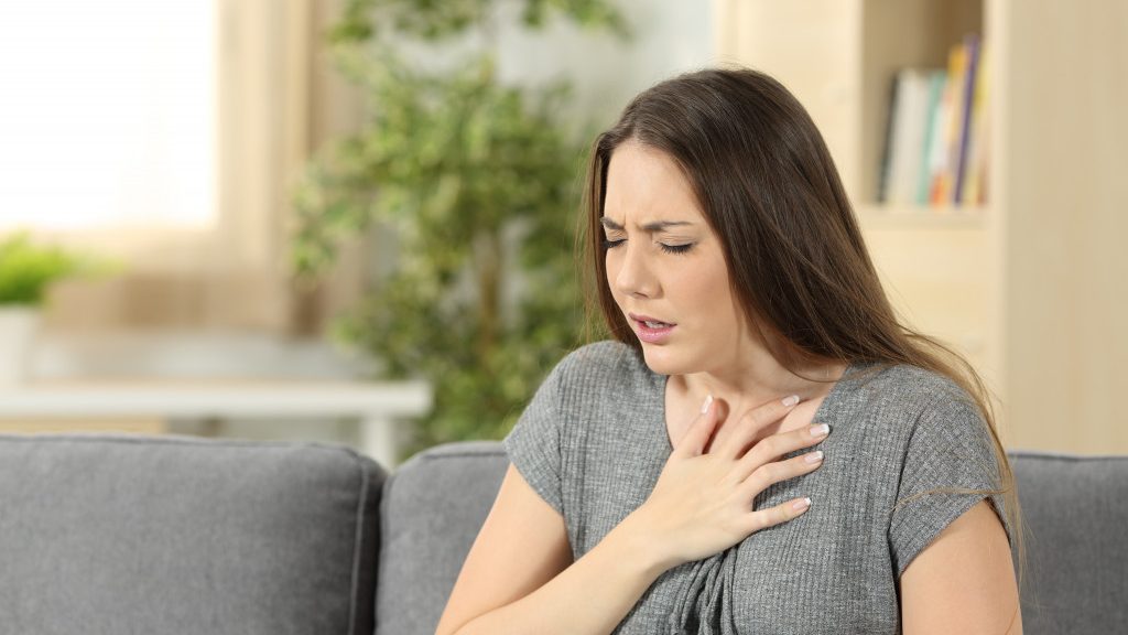 A woman holding her aching chest at home