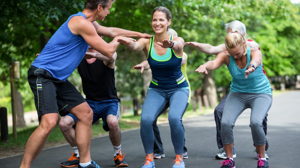 Group of young people exercising at a park with a coach helping them.