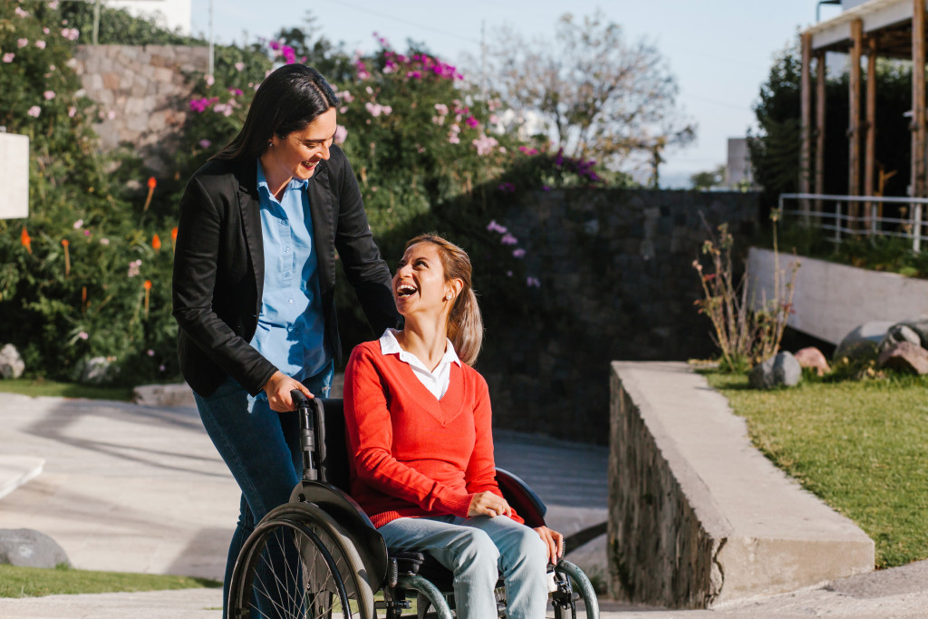happy young woman pushing her friend sitting on a wheelchair