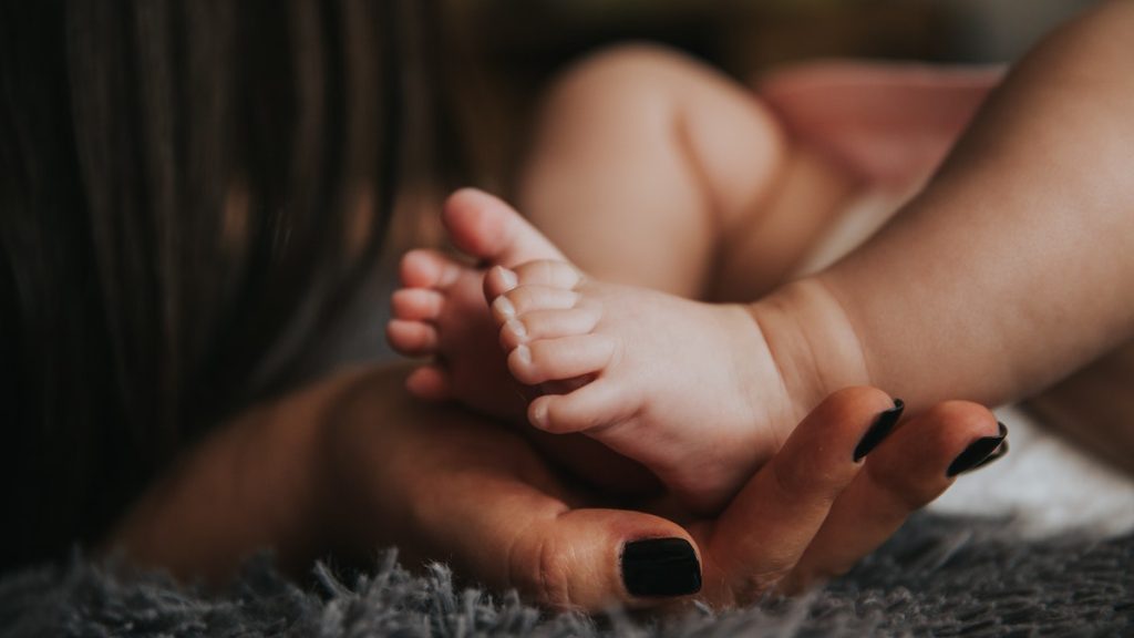 Person Holding Baby's Feet in Selective Focus Photography
