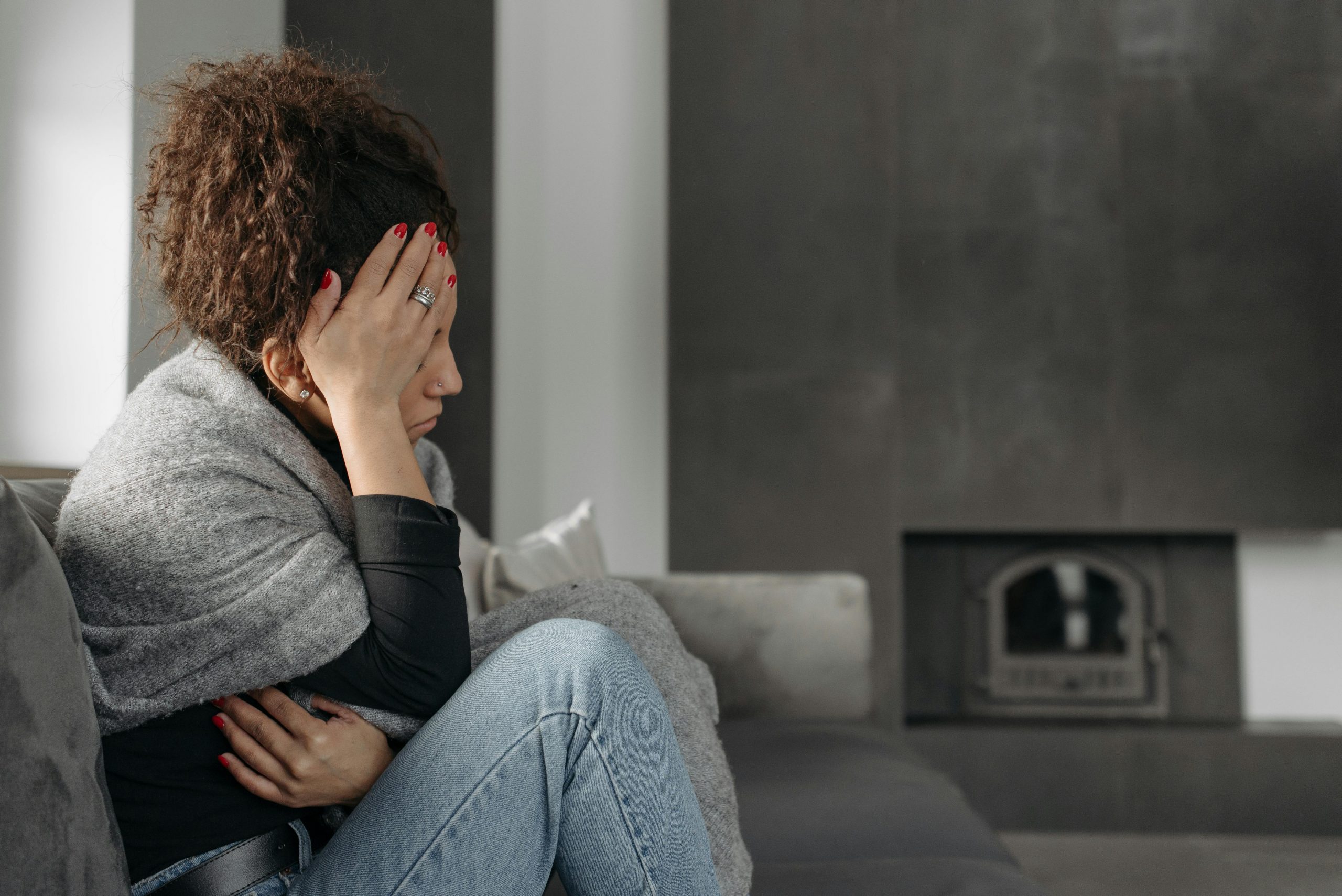 tired-looking woman sitting on a couch, resting her head on her hand