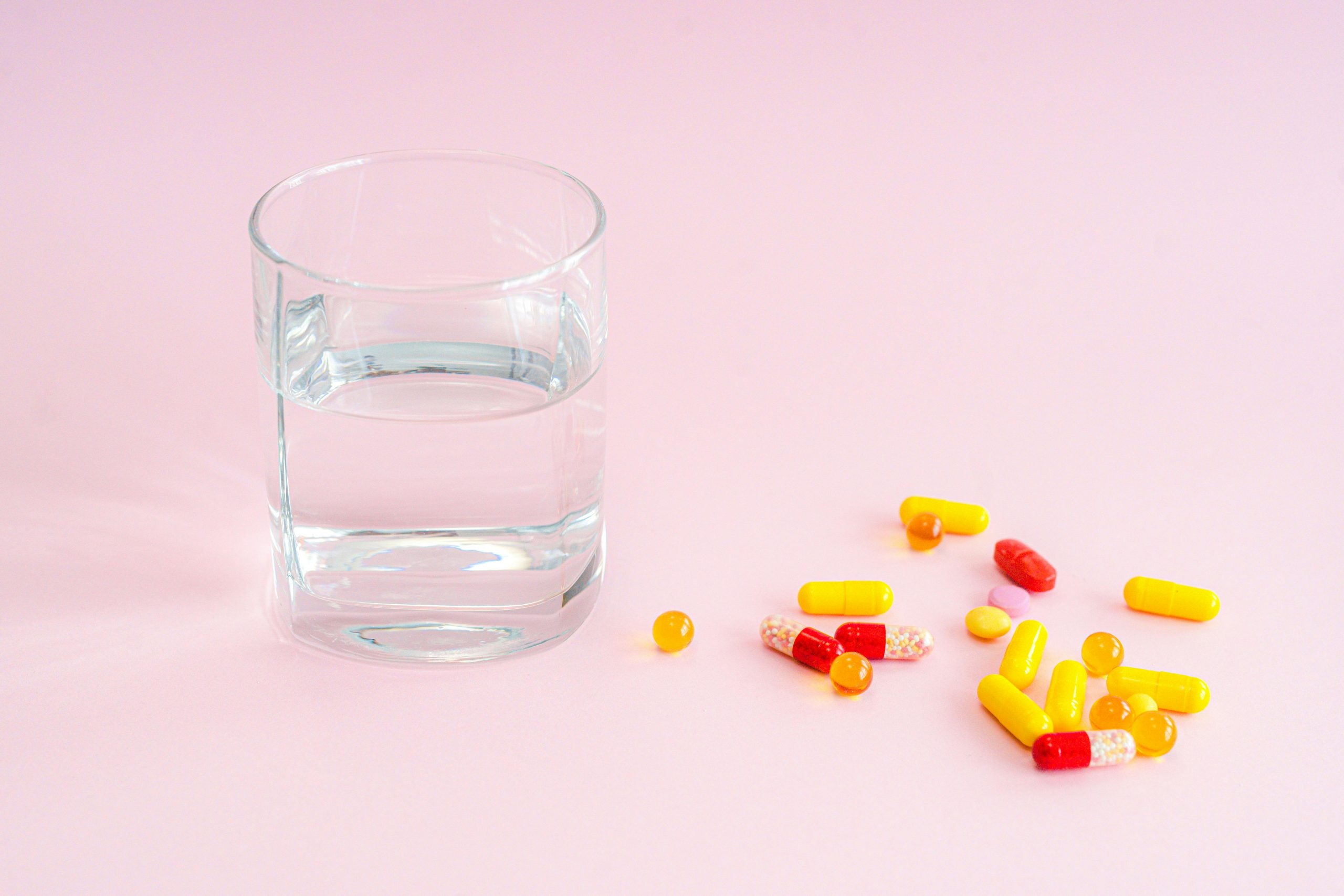 yellow and red pills next to a glass of water