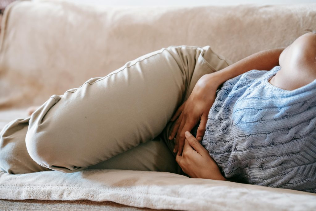 woman in pain lying on a couch, holding her lower abdomen
