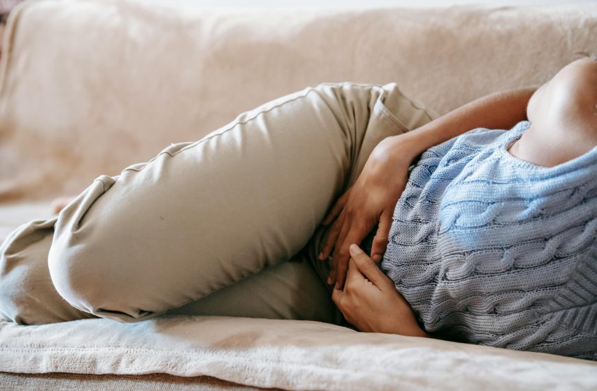 woman in pain lying on a couch, holding her lower abdomen