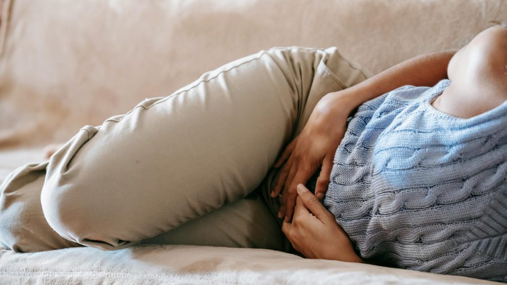woman in pain lying on a couch, holding her lower abdomen